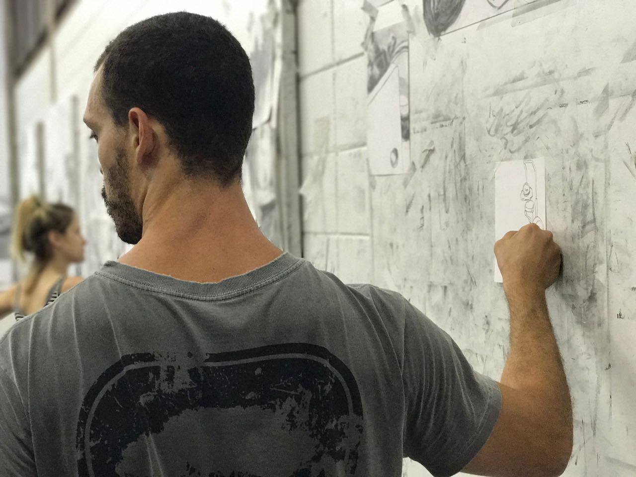 Artista trabalhando em desenho preso na parede do ateliê.